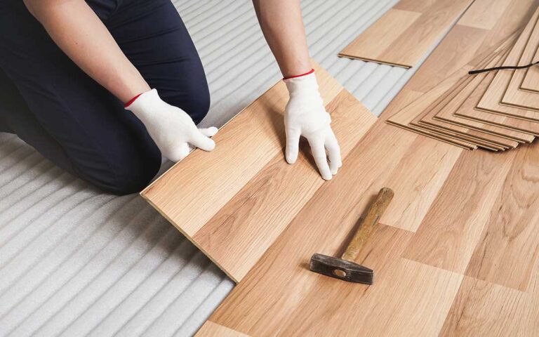 Homeowner comparing flooring samples beside a bright kitchen and adjoining living room